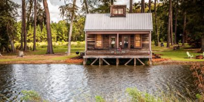 Scenic view of the exterior of a rural rustic wooden camp house used for fishing and hunting. The house is located on a large pond 2000cm