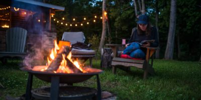 Young woman is reading a book by the campfire late evening at a beautiful canadian chalet 2000-cm